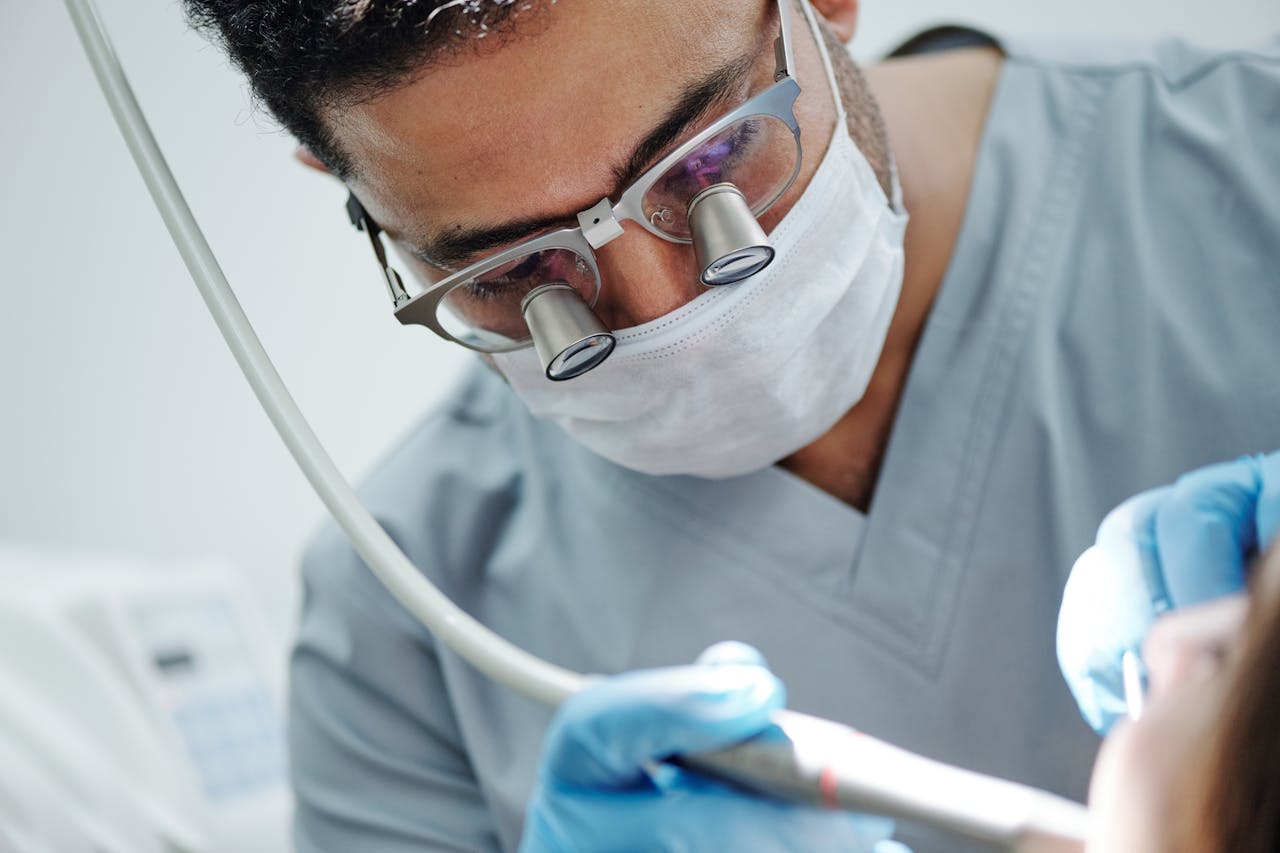 Dentist wearing magnifying glasses performing a dental procedure in a clinic.