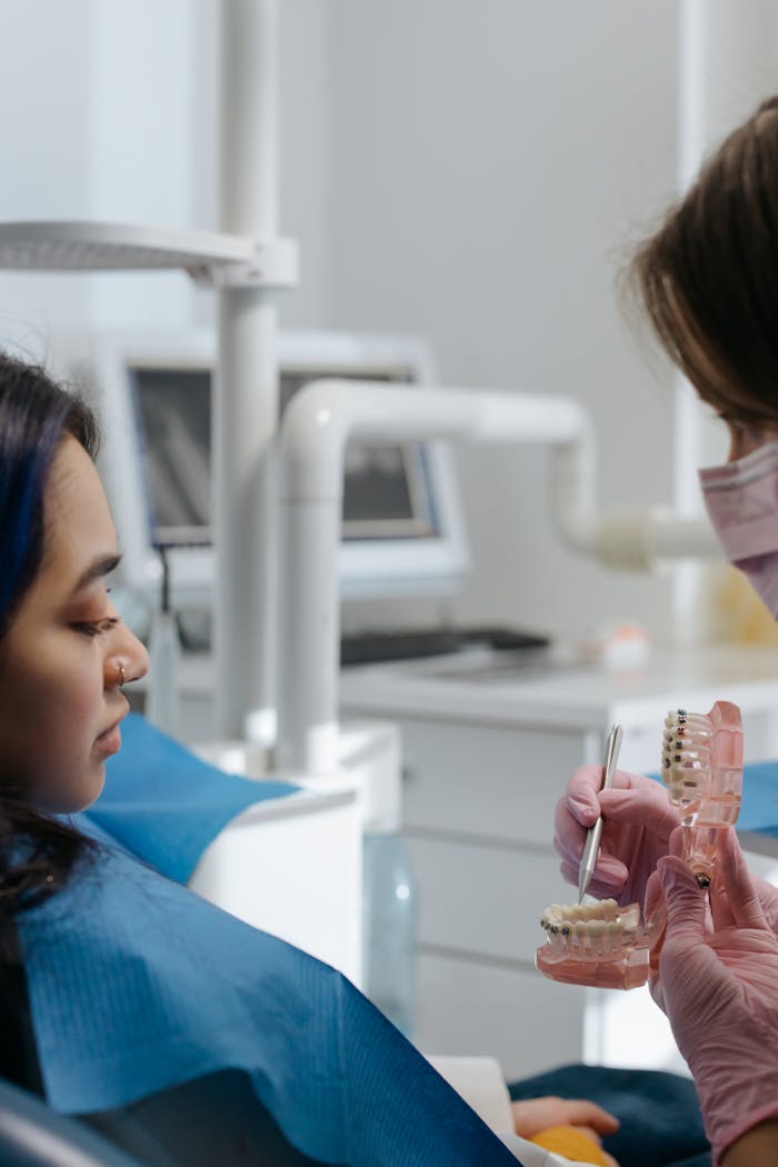A dentist explaining dental procedures using a teeth model during a patient consultation.